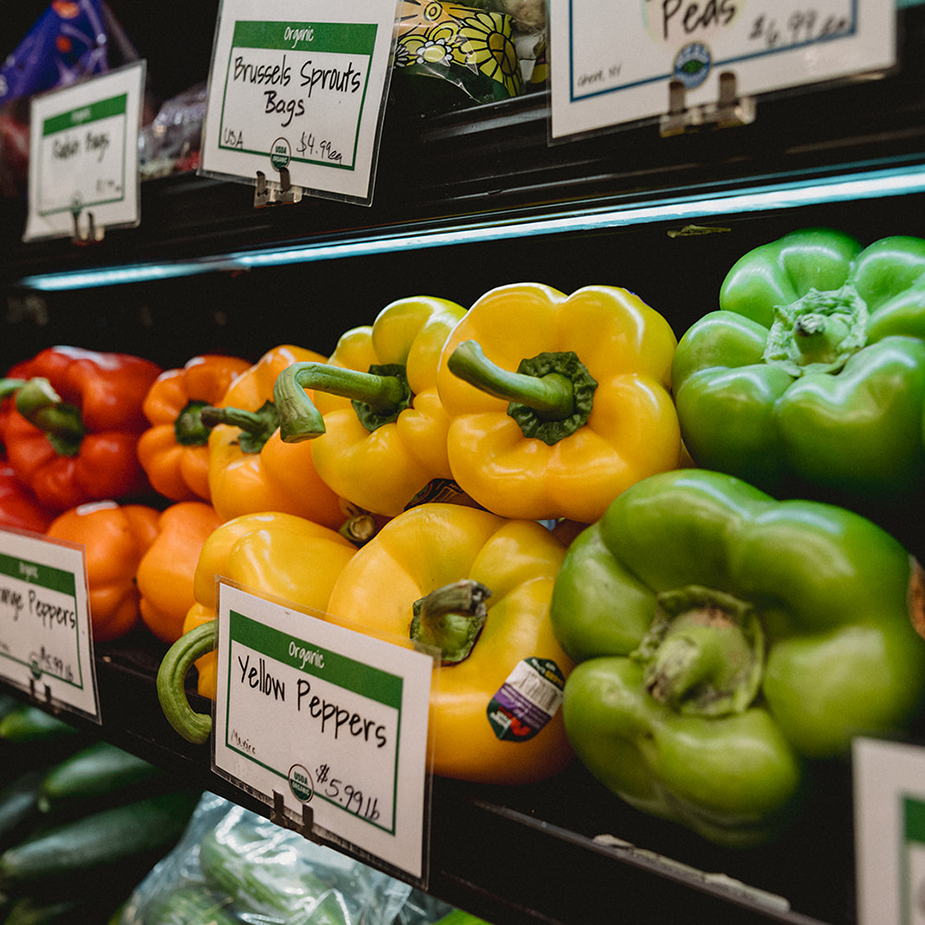 side view of all colored bell peppers stacked on store produce shelf