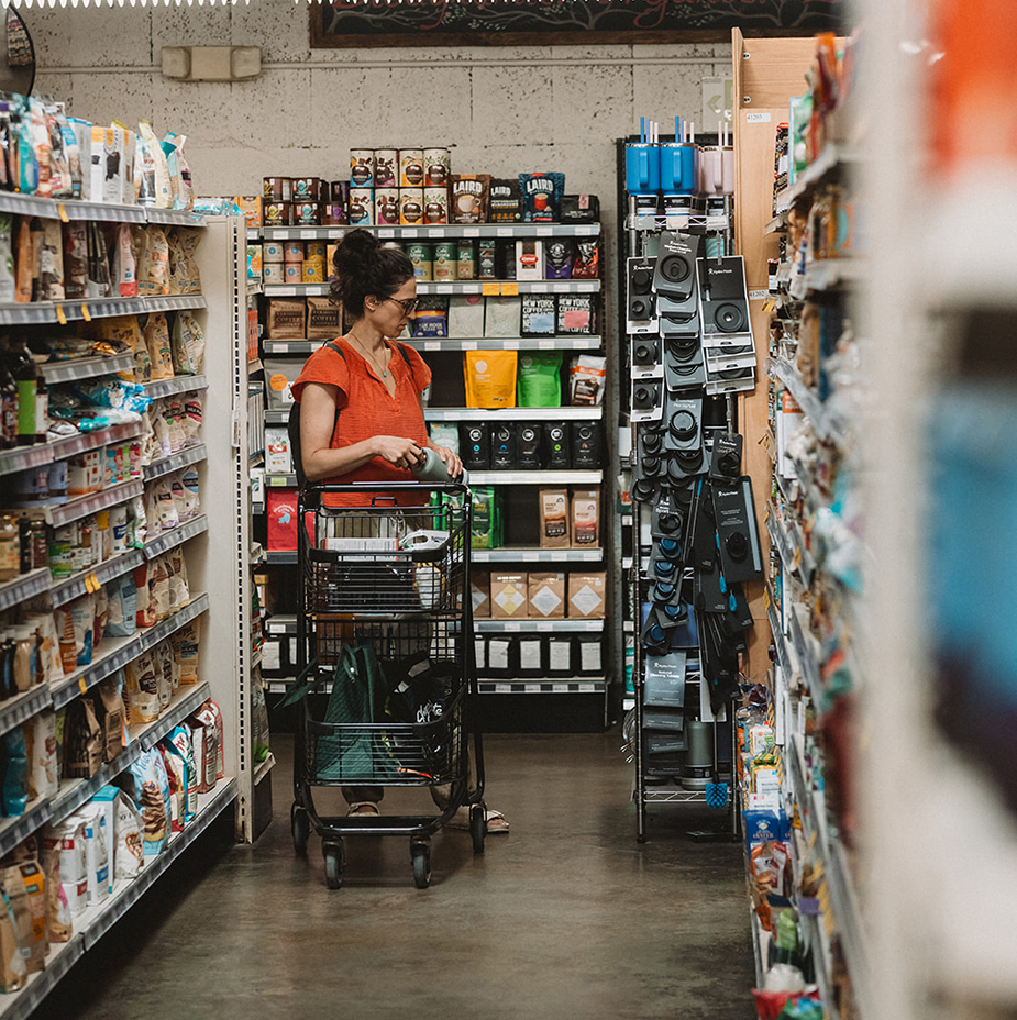 customer at end of aisle with cart looking down at hydro flask bottles while holding one